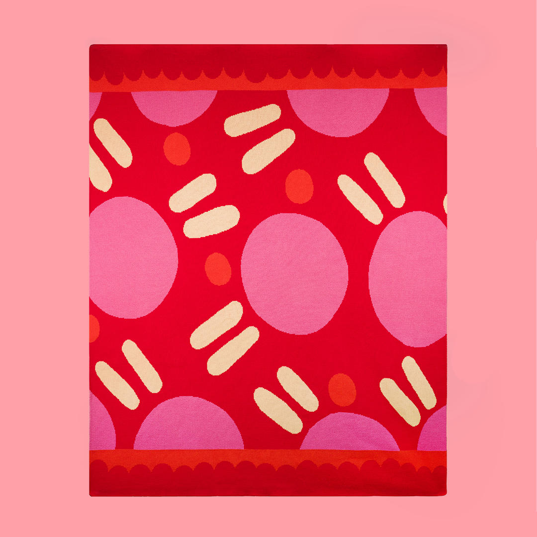Top down view of a pink and red polka dotted blanket on a light pink background.