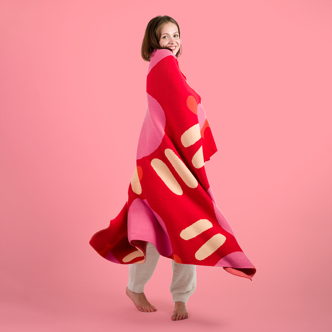 Woman wrapped in a red and pink polka dotted knit blanket twirling around.