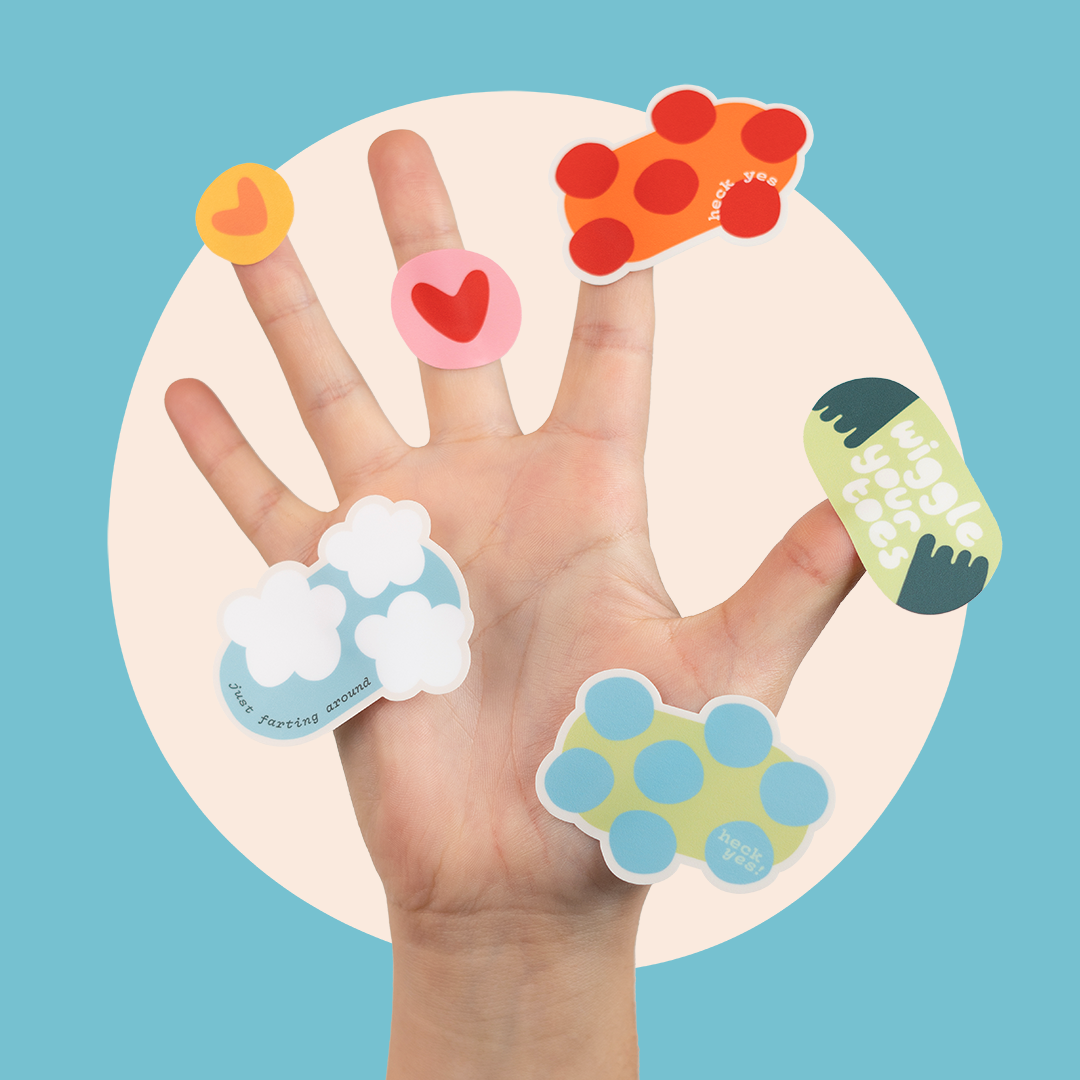 Hand spread out with various colorful stickers stuck all over the fingers. Each sticker is a different shape and has phrases like "just farting around" or "heck yes" and "wiggle your toes"