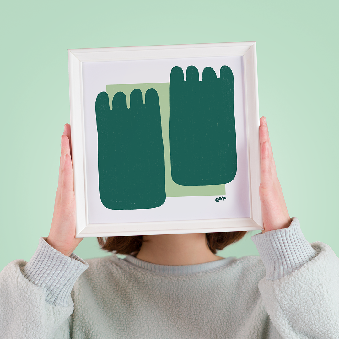 Woman holding a white framed print of two dark green squid shapes on a mint green square.