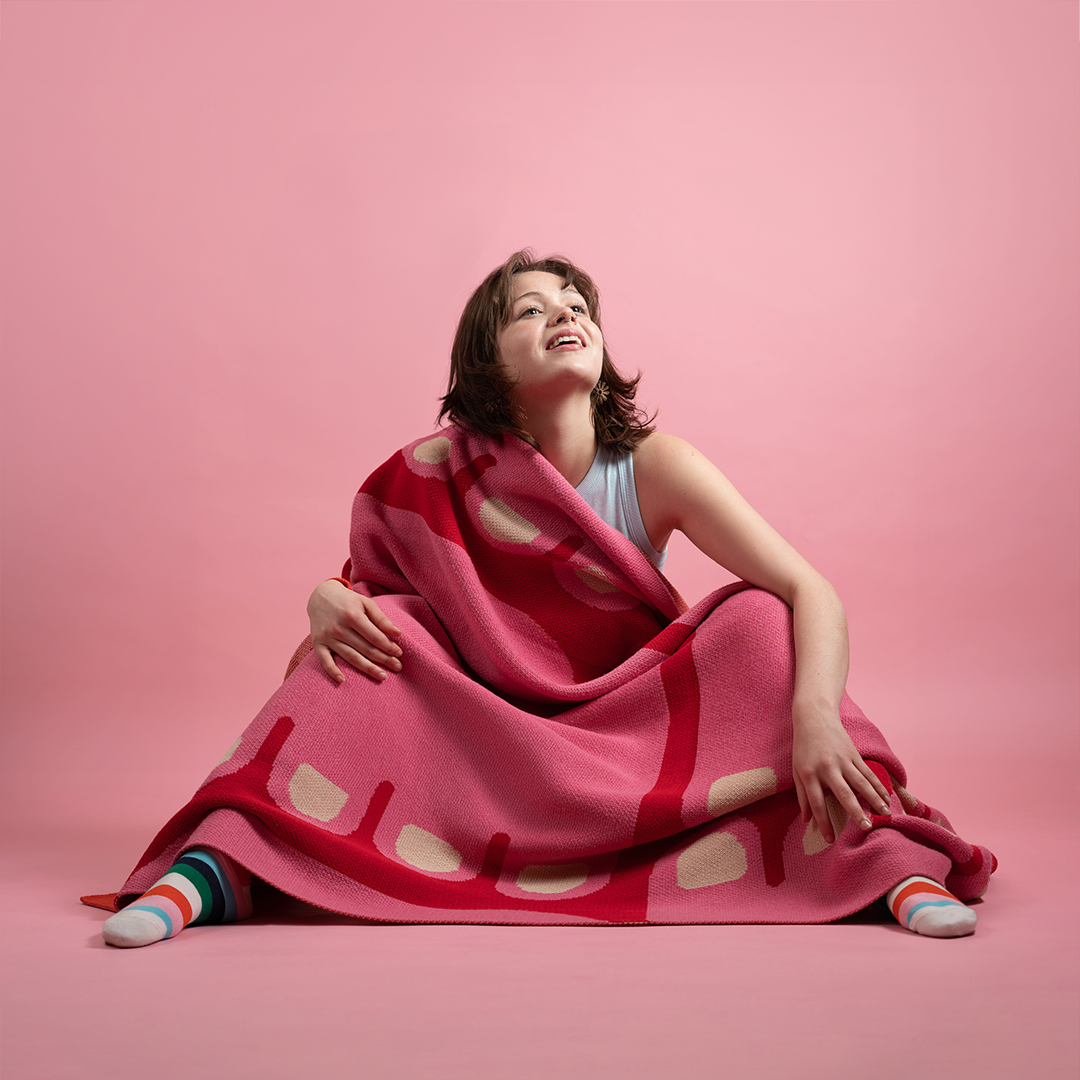 Woman sitting on the floor wrapped up in a red and pink blanket.