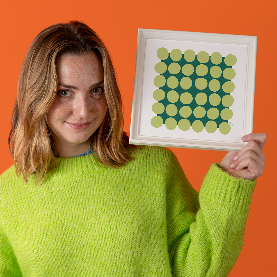 Woman holding white frame with green polka dotted art print in one hand.