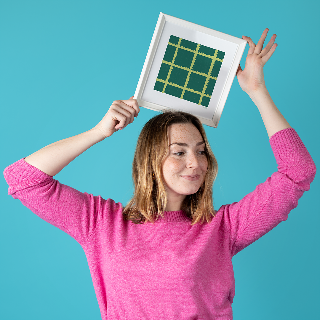 Woman holding white framed print of a green and dark green plaid grid.